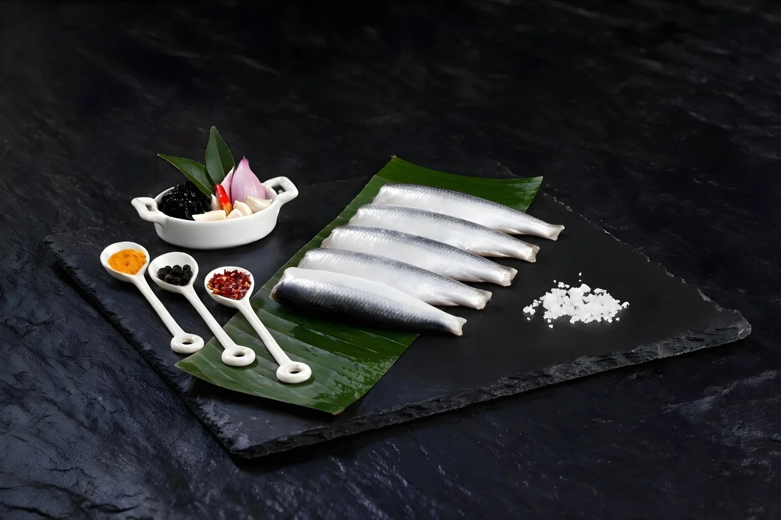 Five whole cleaned sardines on a banana leaf with spices