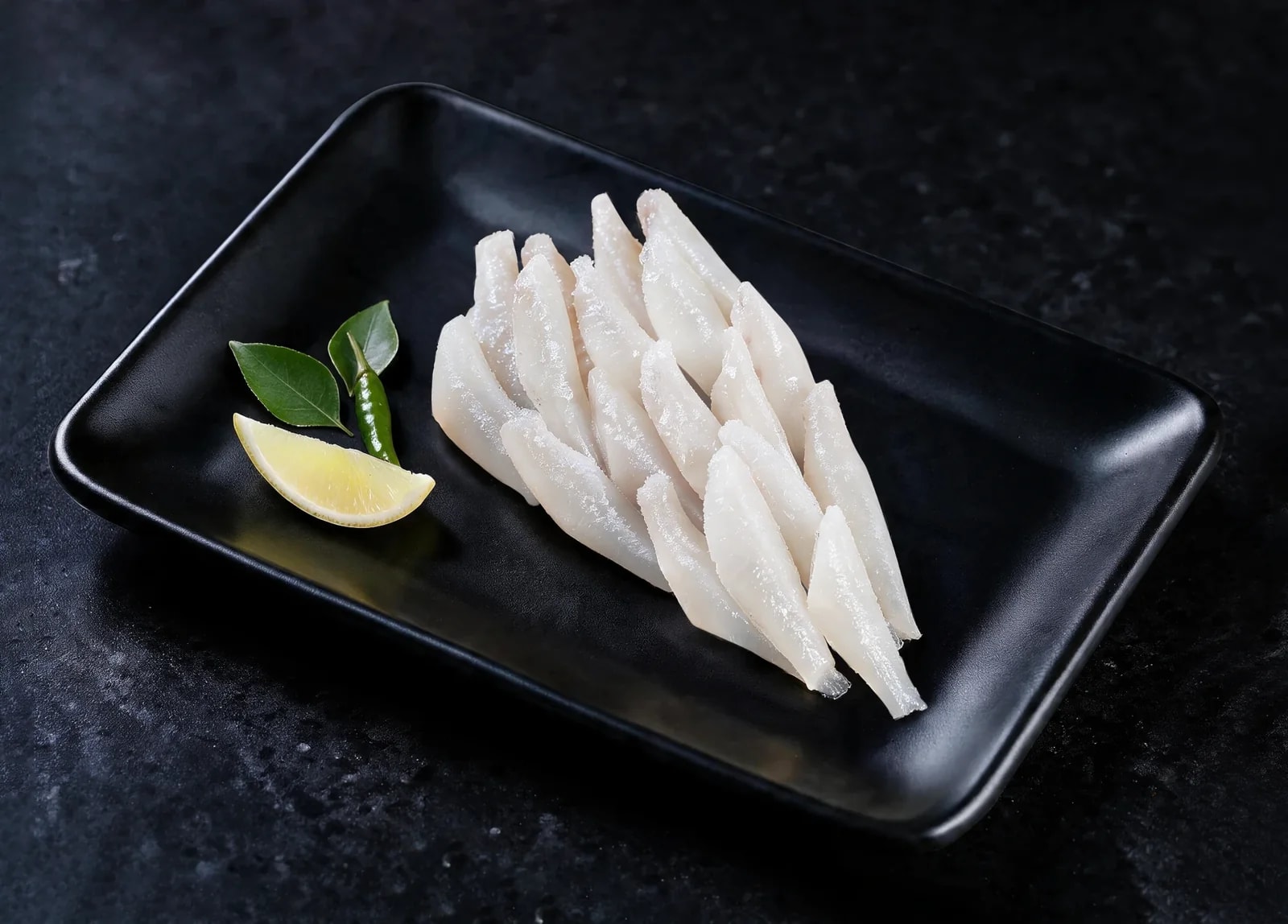 Boneless white fish strips on a black tray with lemon